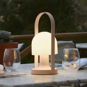 Marset Follow Me bordlampe på et udendørs spisebord en hyggelig aften, og spreder et varmt, blødt lys.