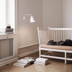Hvid Caravaggio væglampe fra Fritz Hansen placeret ved en hyggelig læsekrog med træbænk.