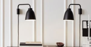 To sorte Caravaggio væglamper fra Fritz Hansen i et minimalistisk interiør med lyse vægge og mørke detaljer.